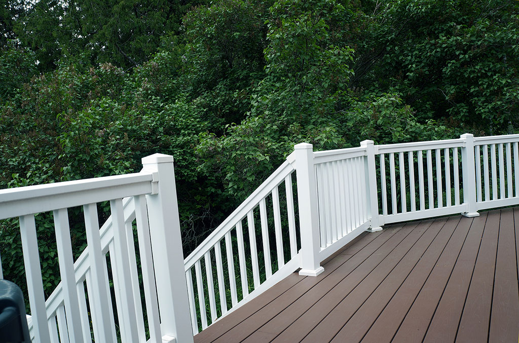 A Wooden Deck With White Vinyl Deck Railing With Stairs in Front of a Large Tree
